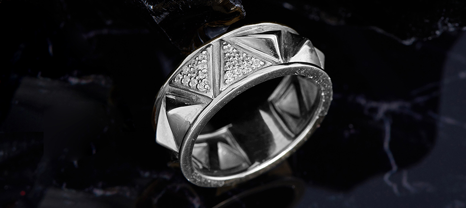 Anel de platina ornamentado com padrões triangulares e acentos de diamante, exemplificando opções de joias duráveis na comparação de metais.