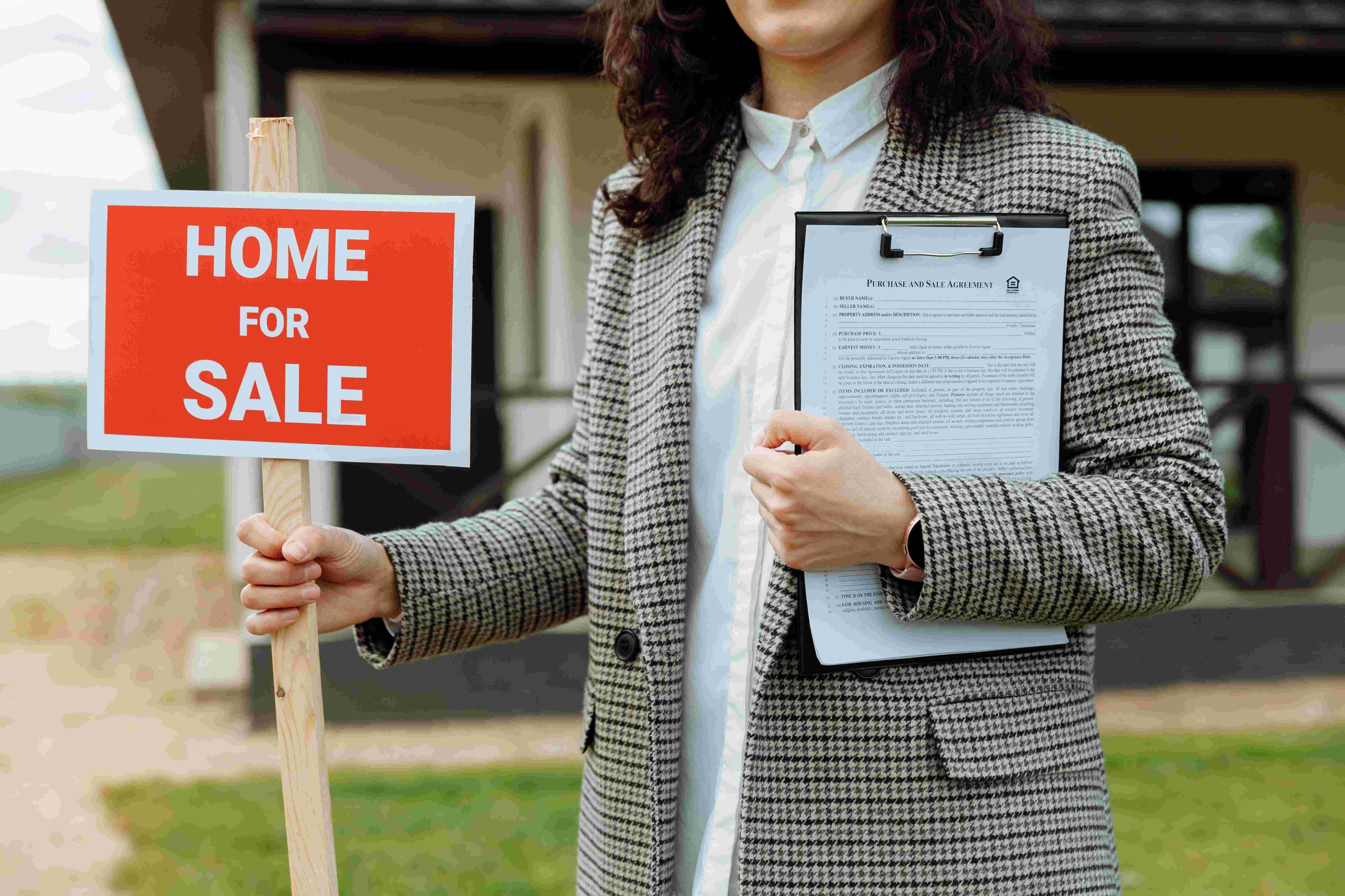Person holding a “Home for Sale” sign and purchase agreement in front of a house, illustrating selling a home without a realtor.