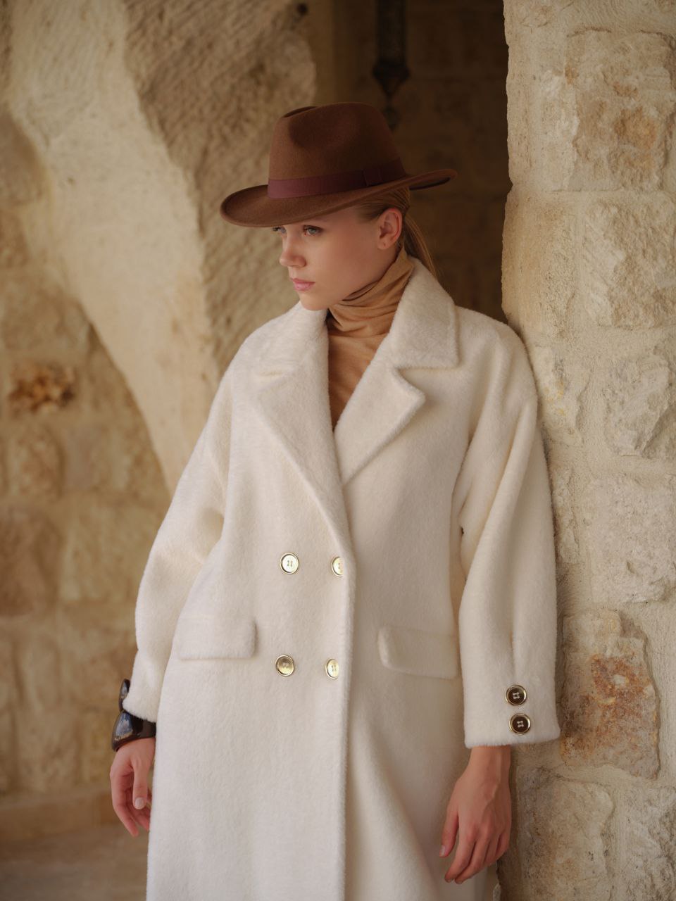 Woman in vintage-style winter coat and brown hat, suitable for 50's themed vacation.