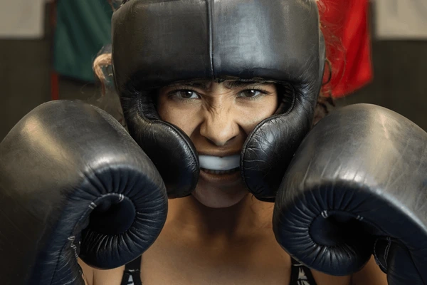 Boxer wearing a padded helmet, mouthguard, and gloves, showcasing essential boxing gear in an intense stance for the sport.