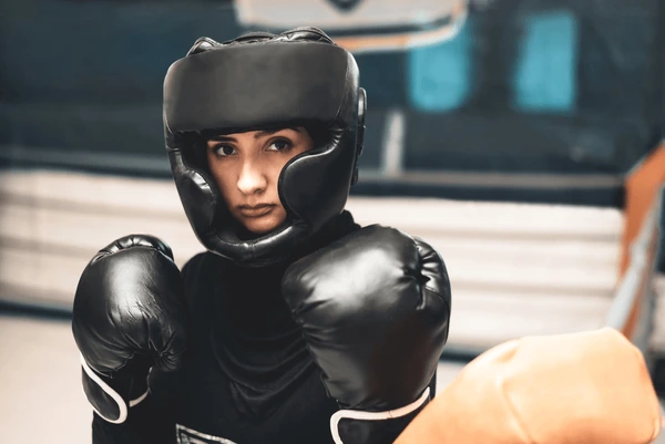 Boxer wearing black gloves and headgear, showcasing essential boxing gear in a gym setting.