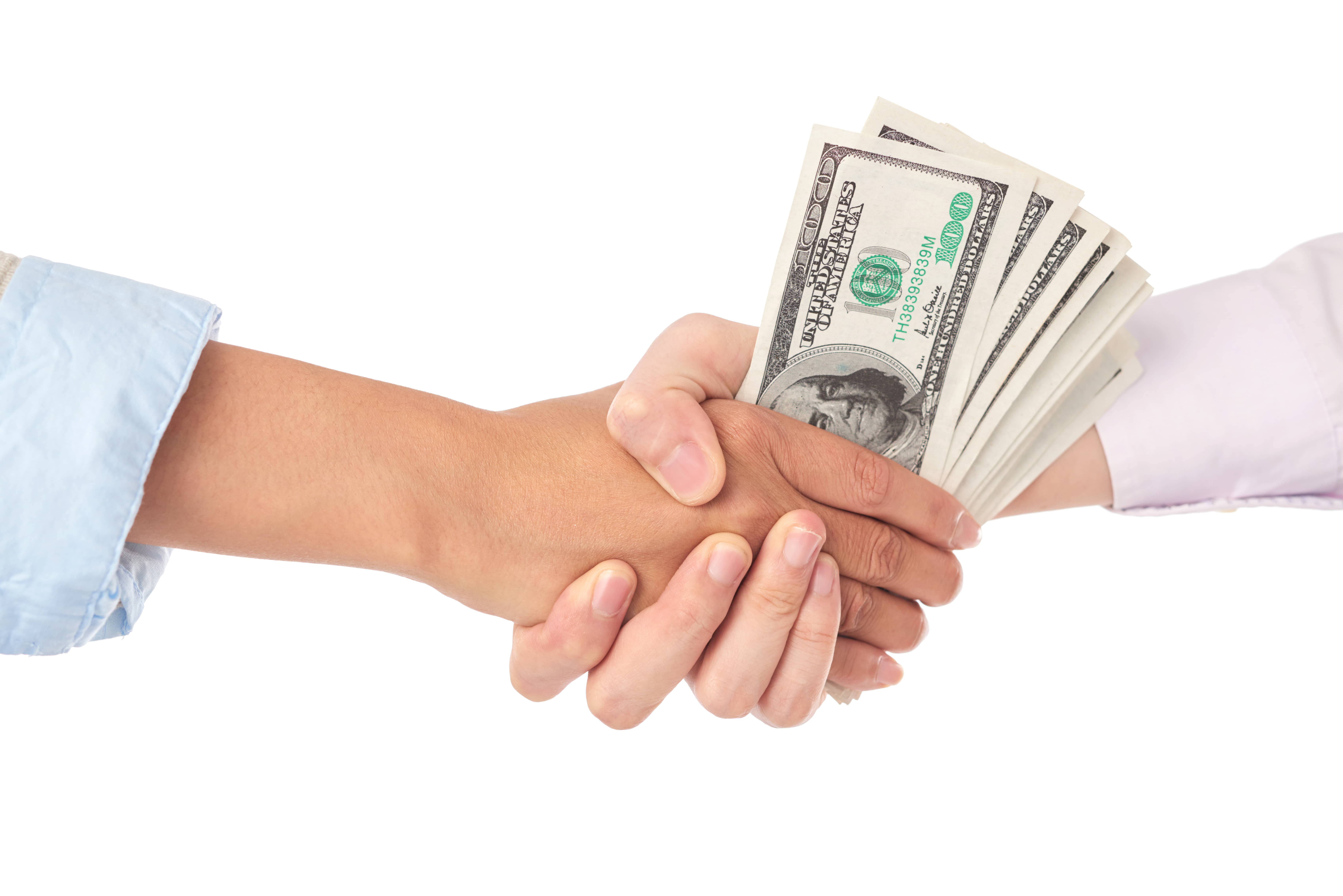 A handshake with one person holding a stack of hundred-dollar bills, symbolizing a successful home sale transaction.