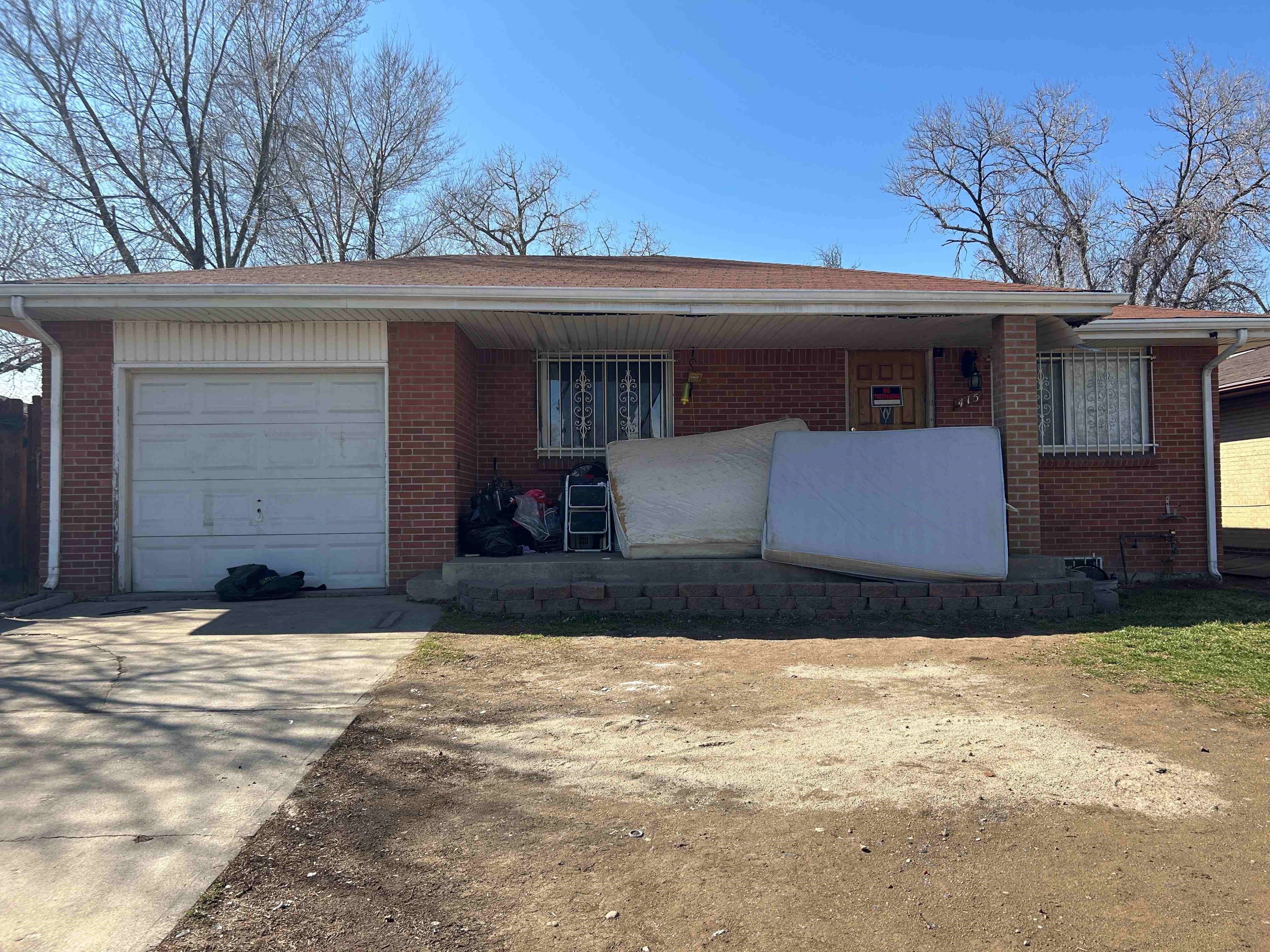 Front view of an old brick house with cluttered items, including mattresses, on the porch, highlighting challenges in preparing old homes for sale.