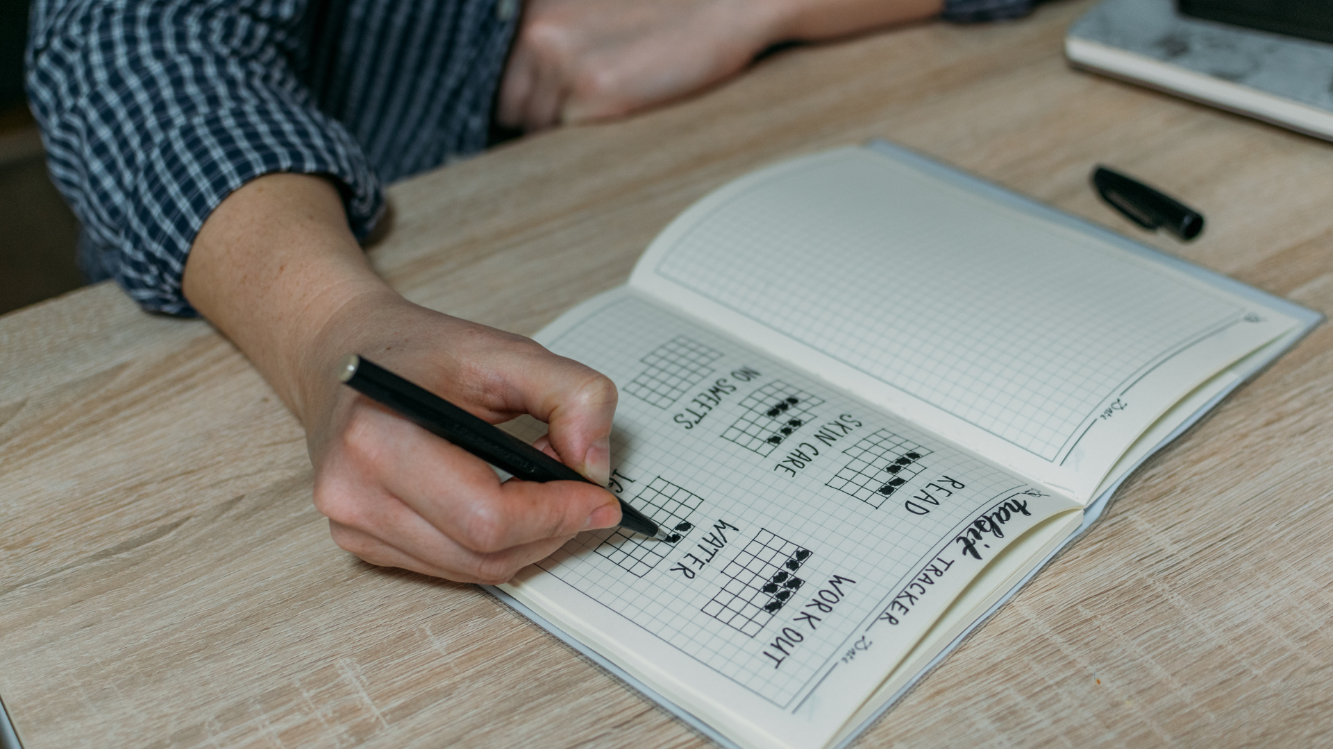 Person writing a workout plan in a notebook, planning gym sessions.