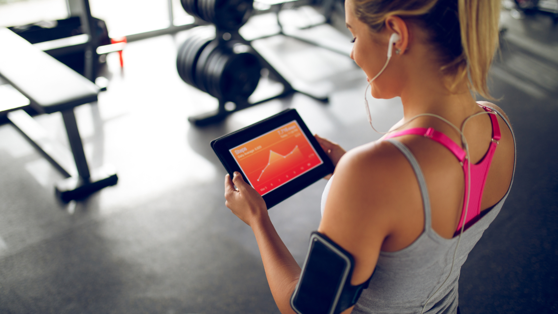 Woman with tablet displaying workout stats in a gym.