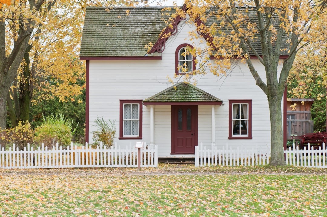 Charming small house with white picket fence and autumn foliage, illustrating the appeal of selling property quickly in various seasons.