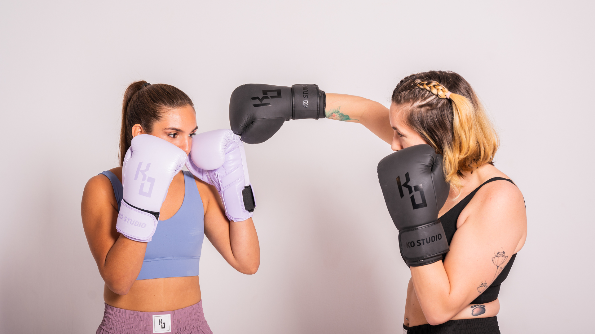 Two women practicing boxing wearing gloves in a gym setting.