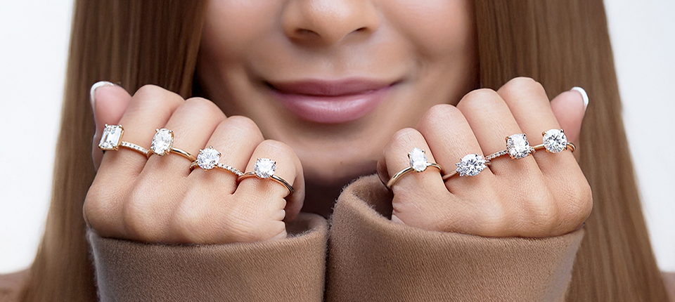 Woman showcasing hands adorned with various diamond engagement rings, highlighting styles and settings for choosing the perfect ring.