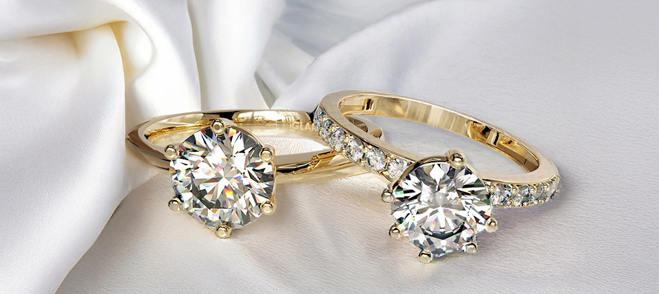 Two gold engagement rings on white silk, each featuring a round-cut diamond; one has a diamond-studded band. Elegant choices for ring style selection.