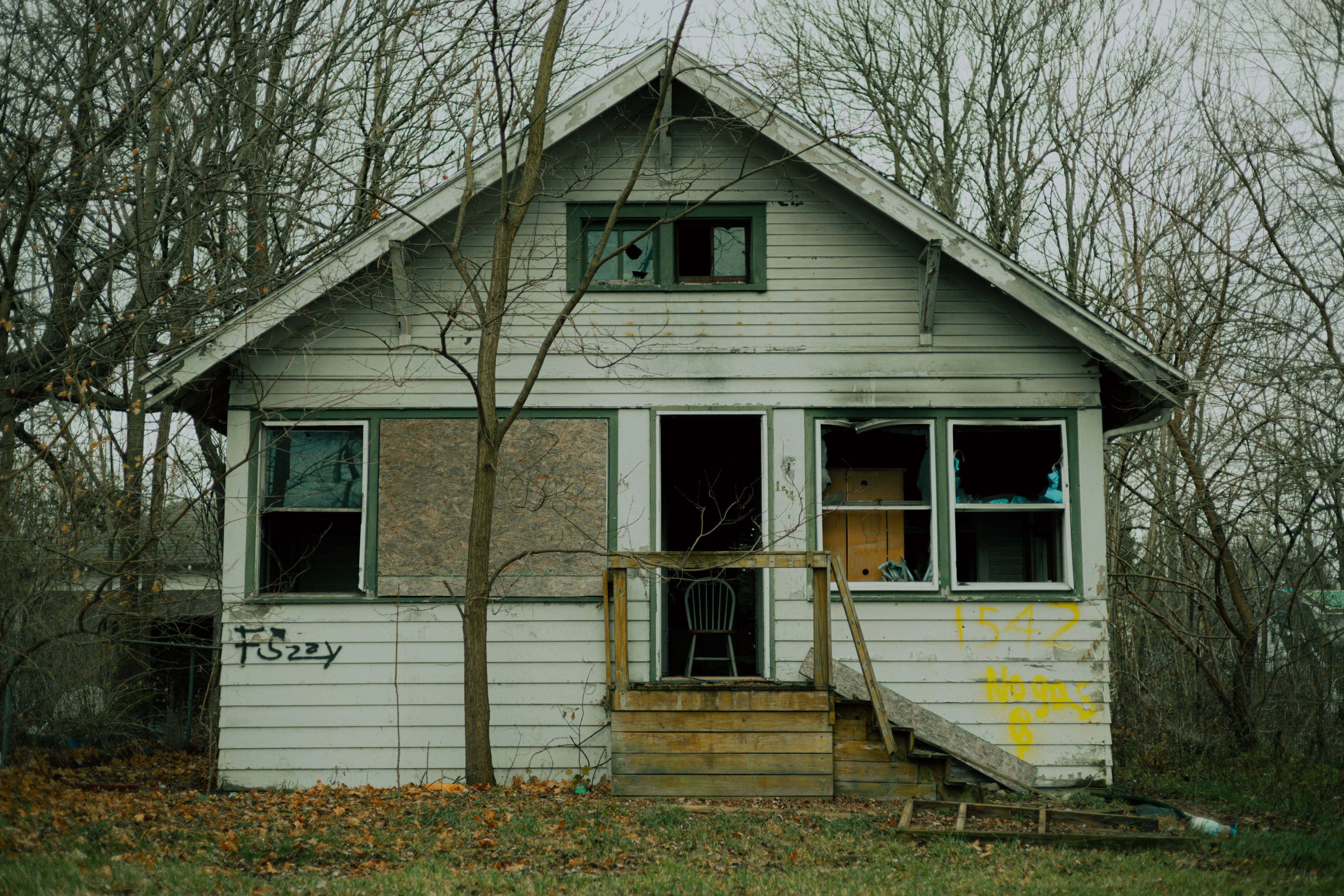 An abandoned house in disrepair, ideal for fix and flip projects in Denver, featuring boarded windows and graffiti on the walls.